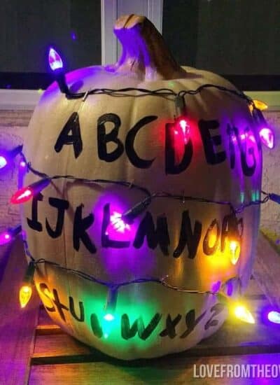 a white painted pumpkin with the alphabet on it wrapped in colorful lights