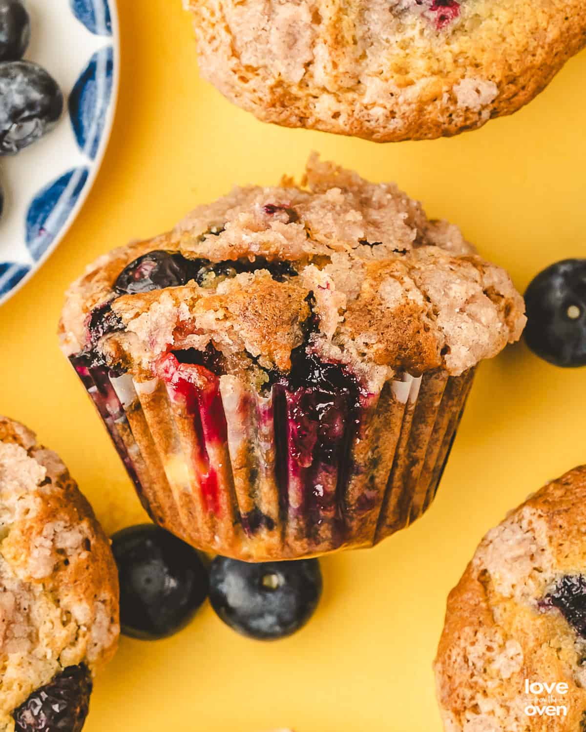 A blueberry banana muffin laying on it's side next to other muffins and blueberries.