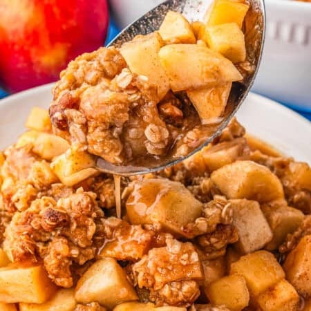 A spoon taking a serving of apple crumble from a plate