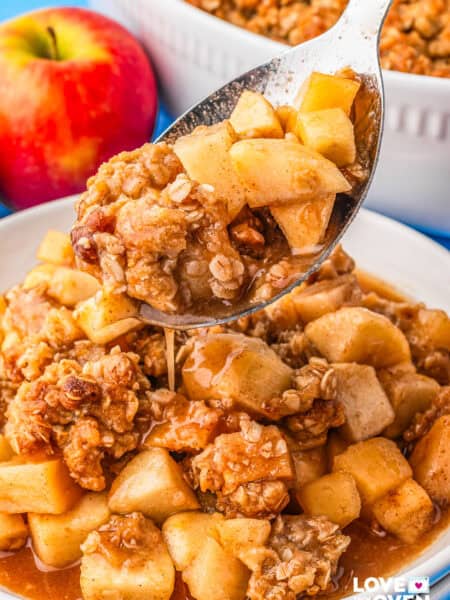 A spoon taking a serving of apple crumble from a plate