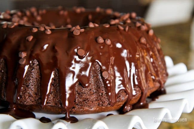 Photo of a chocolate Bundt Cake with chocolate ganache and chocolate chips sitting on a white fluted plate