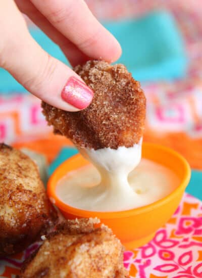 A piece of pull apart bread being dipped in frosting.