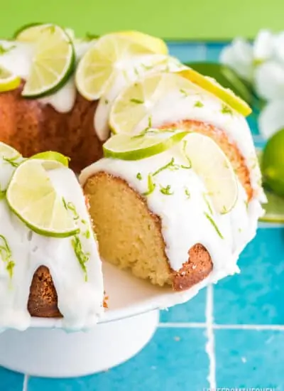 A lime cake on a cake stand with a glaze and lime slices on top.