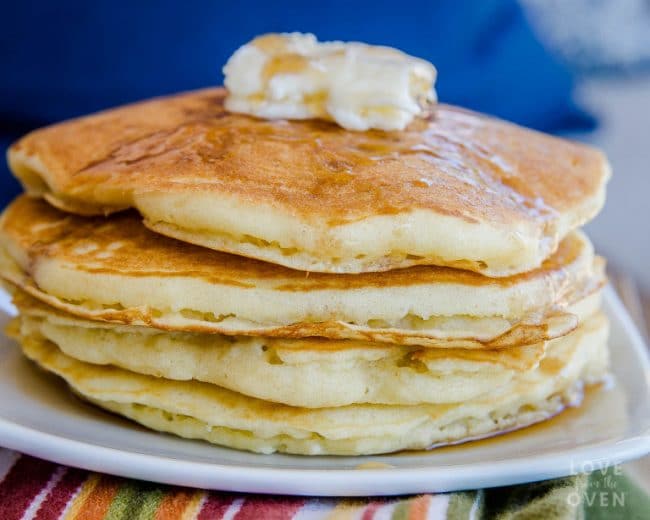 Four pancakes topped with butter and syrup sitting on a white plate made with a fluffy pancake recipe 
