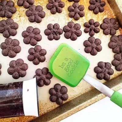 Chocolate spritz cookies on a baking tray with a green spatula