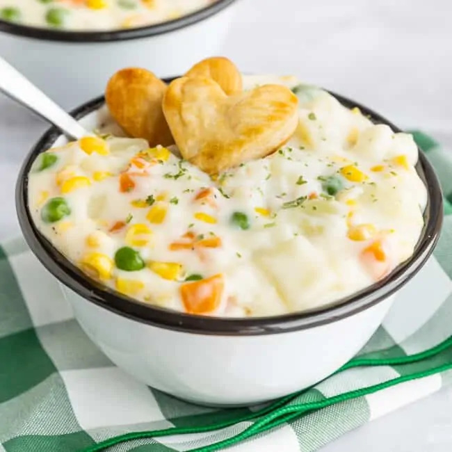 a bowl of pot pie soup with two heart crackers on top