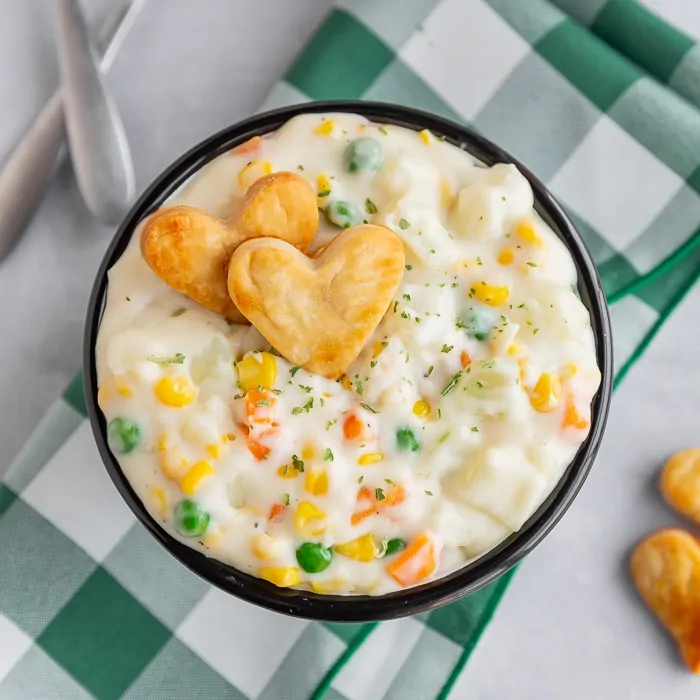 Bowl of pot pie soup with carrots peas and corn, topped with heart shaped pie crust pieces