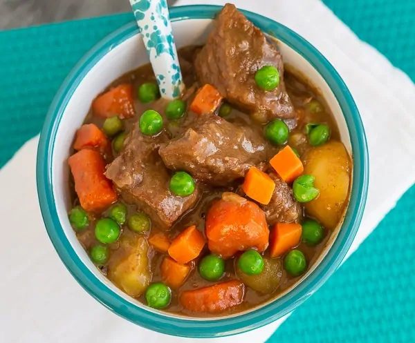 bowl of beef stew with green peas and carrots and a spoon