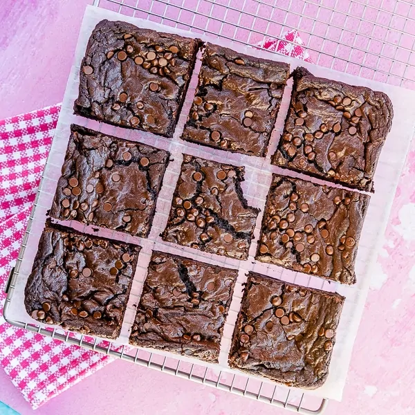 Nine homemade brownies on a cooling tray with a pink background and pink towel