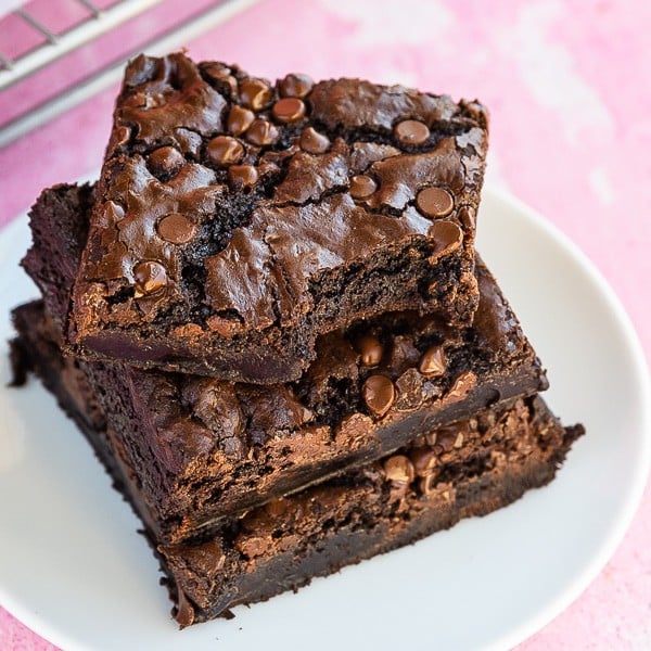 Three chocolate brownies on a white plate with a pink background