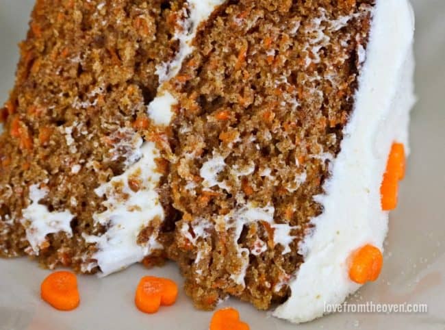 A close up slice of carrot cake with frosting and carrot hearts