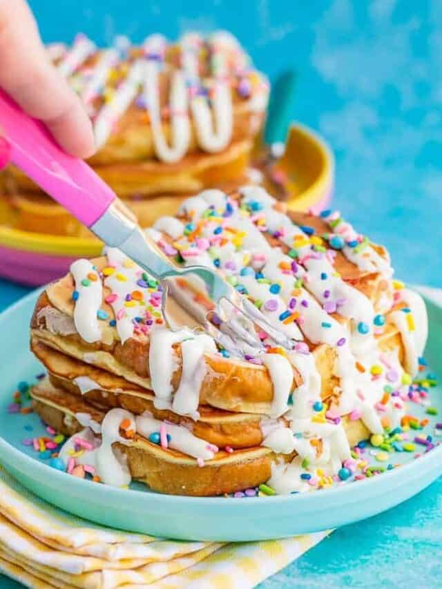 Stack of french toast with frosting and sprinkles being cut by a pink fork