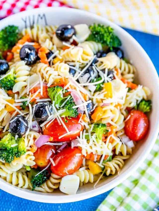 Bowl of pasta salad with tomatoes, olives, broccoli, carrots and cheese