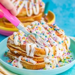 Stack of french toast with frosting and sprinkles being cut by a pink fork