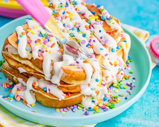 Two slices of French Toast topped with frosting and sprinkles being cut with a pink fork