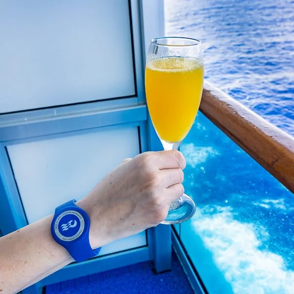 Photo of a hand holding a glass of mimosa while on a cruise ship wearing an ocean medallion 