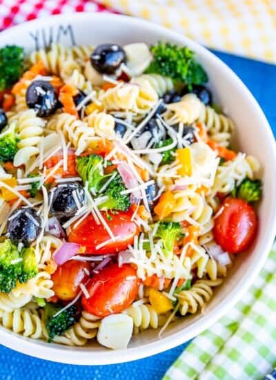 Bowl of pasta salad with tomatoes, olives, broccoli, carrots and cheese