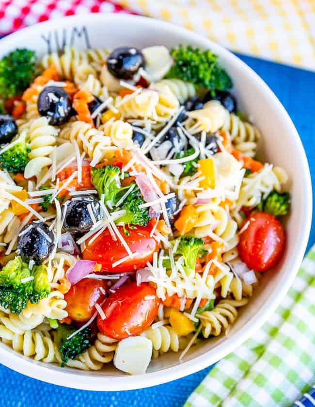 Bowl of pasta salad with tomatoes, olives, broccoli, carrots and cheese