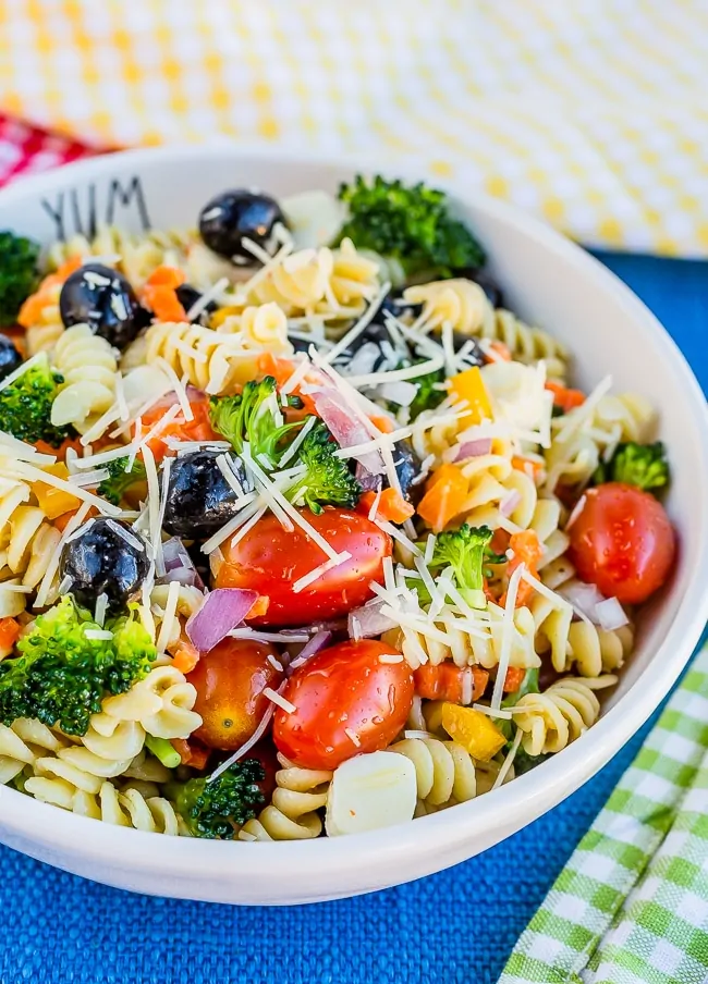 Bowl full of pasta, tomatoes, olives, carrots, broccoli and onions