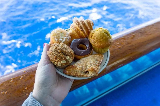 A plate of pastries being held on a blue balcony by blue water on a princess cruise