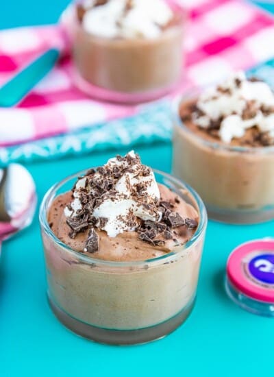 Three containers of chocolate mousse topped with whipped cream and chocolate on a blue background