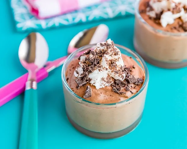 two cups of chocolate mousse next to pink and blue spoons