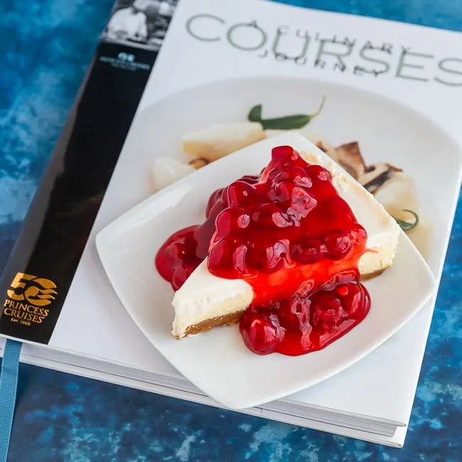 Cheesecake with cherries on top sitting on a cookbook 