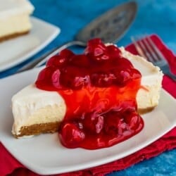Classic cheesecake topped with cherries on a white plate, with a red napkin and blue background