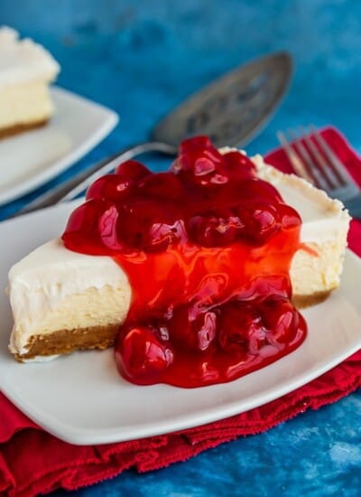 Classic cheesecake topped with cherries on a white plate, with a red napkin and blue background
