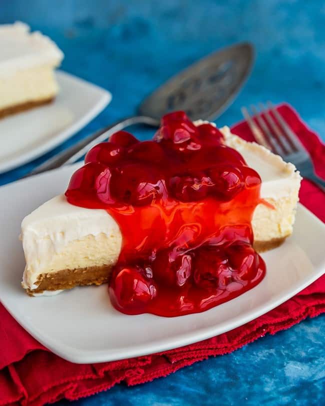 Classic cheesecake topped with cherries on a white plate, with a red napkin and blue background