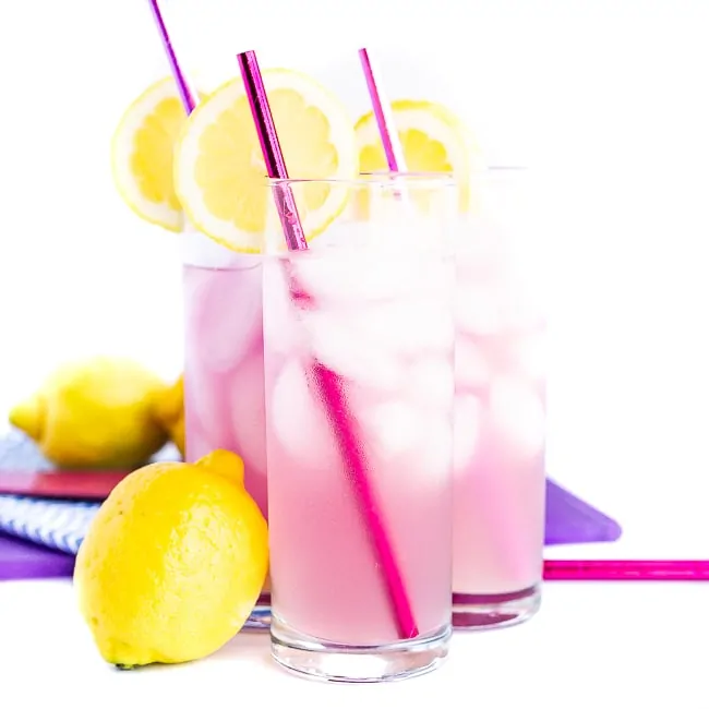 Three pink cocktails with pink straws, lemon slices and a lemon