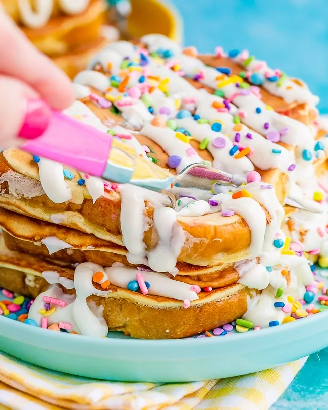 Stack of french toast, with frosting and sprinkles, being cut by a pink fork