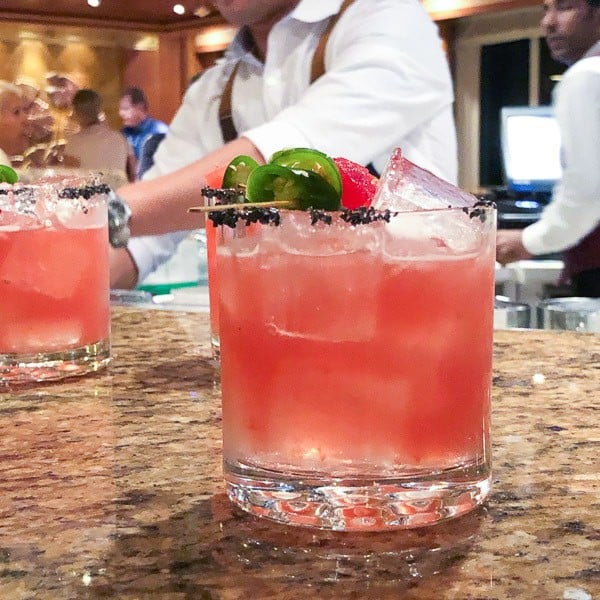 A watermelon margarita sitting on a bar with a bartender behind it