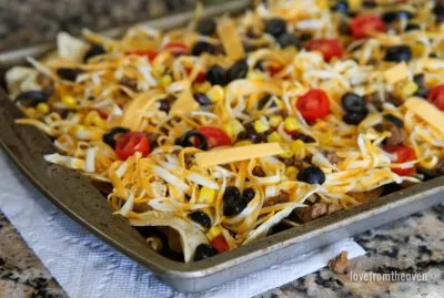 Sheet of uncooked nachos with grated cheese, olives and tomatoes