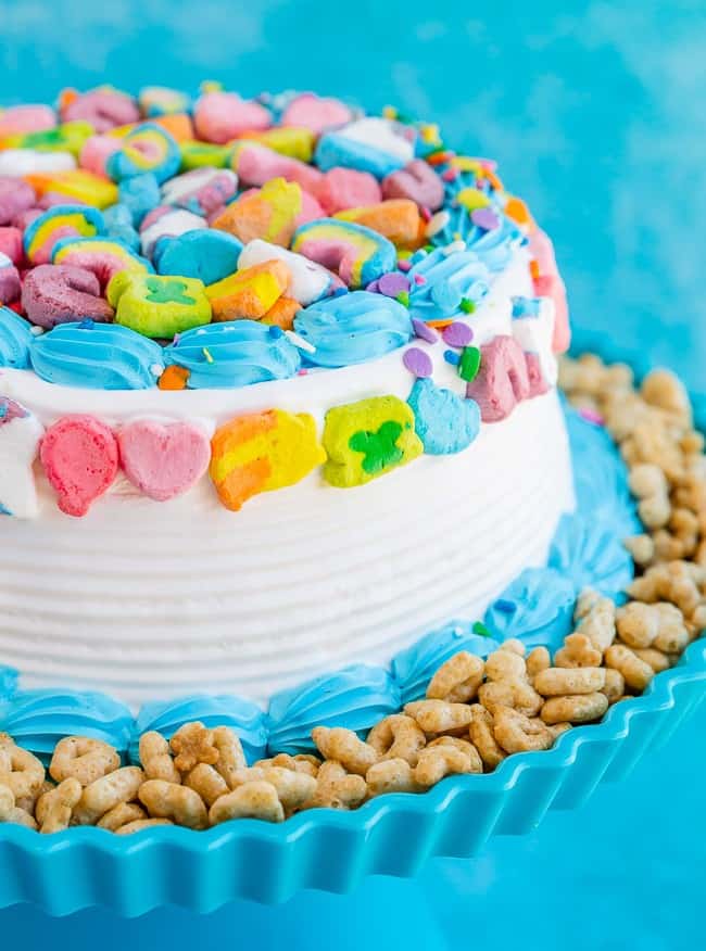 Lucky Charm cake with white and blue frosting, Lucky Charms cereal on the side and Lucky Charms marshmallows on the top
