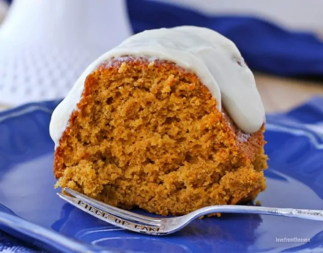 Slice of pumpkin cake with cream cheese frosting on top sitting on a blue plate with a fork