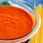 Bowl of San Marzano Tomato Sauce next to pile of uncooked spaghetti noodles