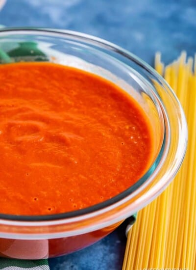 Bowl of San Marzano Tomato Sauce next to pile of uncooked spaghetti noodles