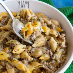 Bowl of cheeseburger macaroni on a blue background with a green napkin