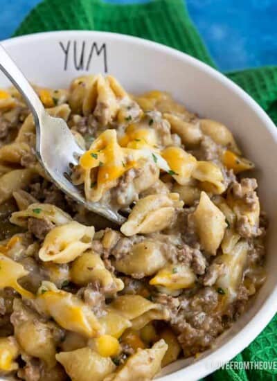 Bowl of cheeseburger macaroni on a blue background with a green napkin