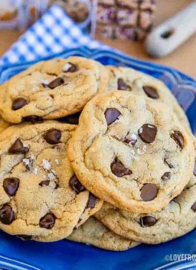 Chocolate chip pudding cookies with sea salt flakes on top, sitting on a blue plate with a blue and white napkin underneath