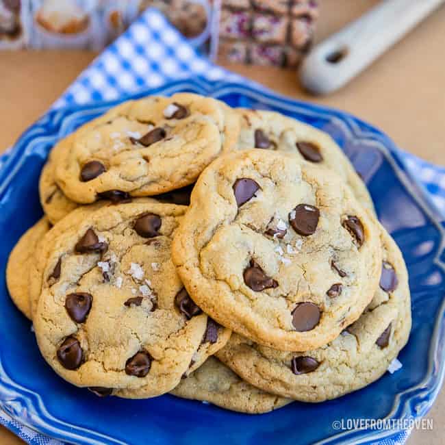 Chocolate chip pudding cookies with sea salt flakes on top, sitting on a blue plate with a blue and white napkin underneath 