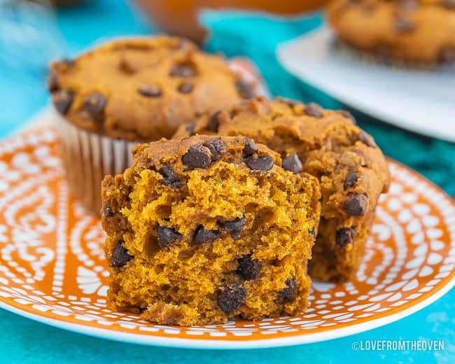A pumpkin chocolate chip muffin broken in half, on an orange plate with a blue background