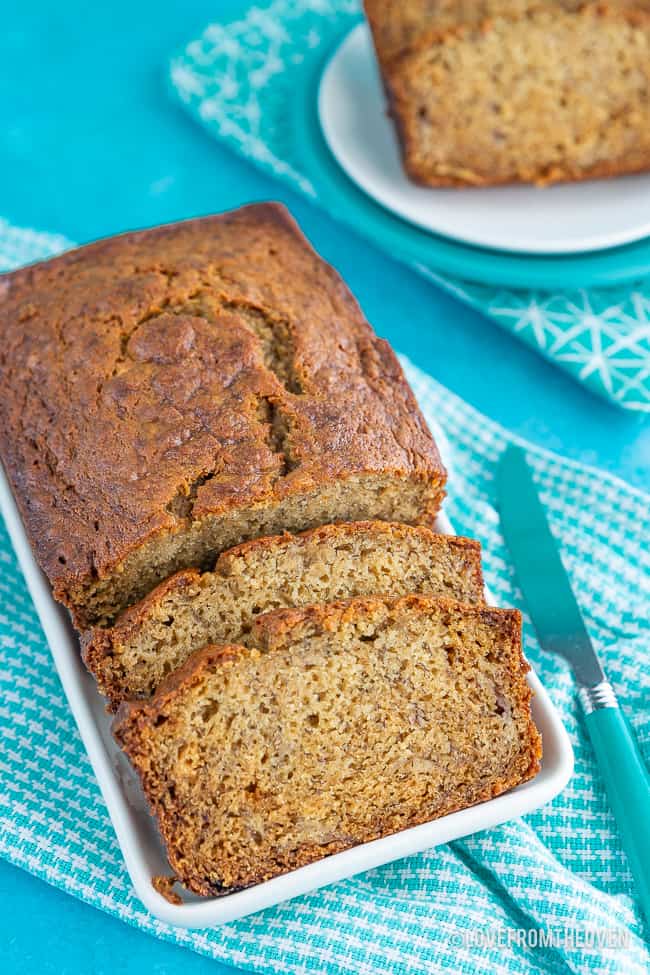 Loaf of banana bread with two slices cut out, sitting on a blue background with a blue check napkin 