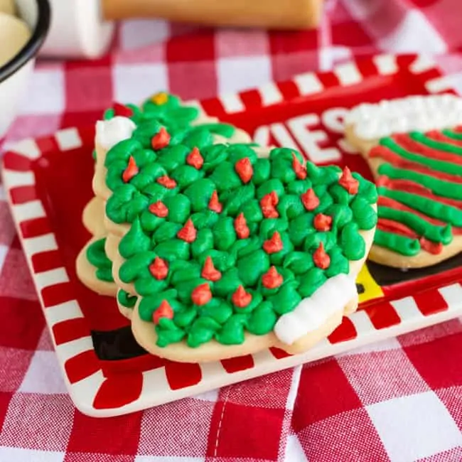 A Christmas tree shaped sugar cookie covered in green frosting on a red plate