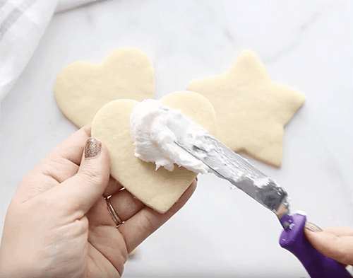 A heart shaped sugar cookie being frosted