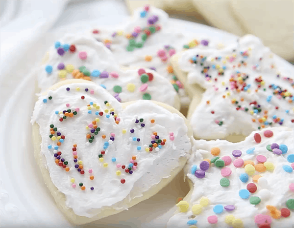 A plate full of frosted sugar cookies with sprinkles