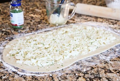 Garlic roll dough rolled out and covered in cheese and seasonings