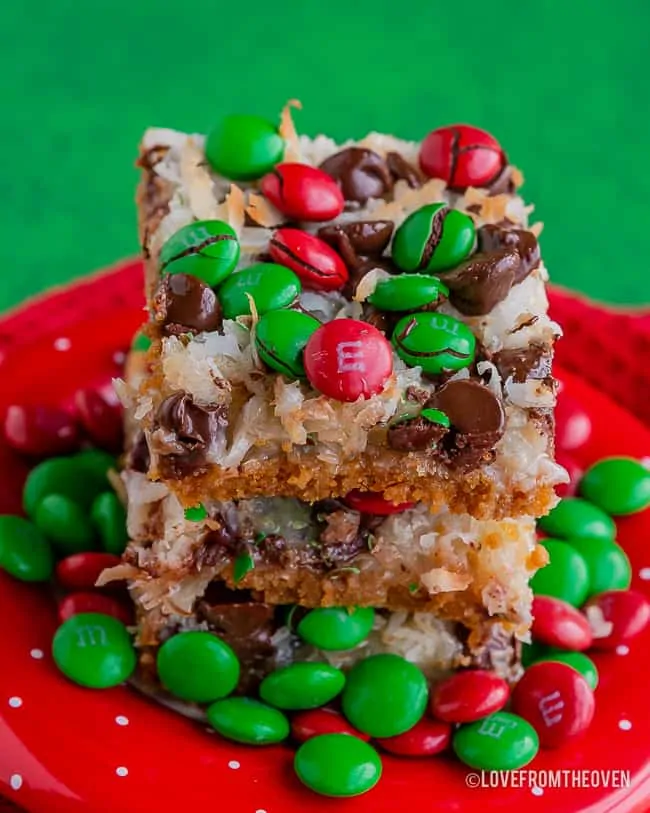 Stack of magic cookie bars covered in M&Ms on a red plate