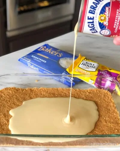 Sweetened condensed milk being poured onto crushed graham crackers